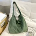 Gros plan sur le sac porté épaule en suédine vert foncé avec texture douce sur canapé. - Vert
