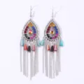Close-up of bohemian drop earrings with colorful rhinestones, metal filigree and dangling chains. - Colorful