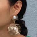 Close-up detail shot of the elegant gold sunburst pearl drop earrings showcasing intricate texture. - Gold