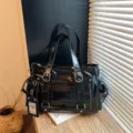 Primo piano della borsa a tracolla utility nera lucida con fibbie e tasche laterali. - Nero