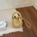 Nahaufnahme einer stylischen gelben Beuteltasche mit geflochtenem Griff auf kuscheligem Teppich. - Basisstil / Gelb