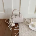 Detailed shot of chic beige pillow handbag with cute puppy charm and stylish pebbled texture. - With Pendant / Off White