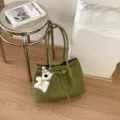 Detail shot of green woven leather tote bag showcasing texture, strap, and cute bear pendant. - Green With Keychain