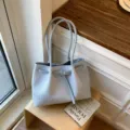 Light blue woven tote bag with double handles and front buckled strap design for daily commute. - Blue