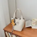 Minimalistische beige emmertas detailweergave met draaisluiting en schattige paardhanger. - Met Hanger / Broken Wit