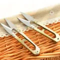 Close-up view of stainless steel U-shaped thread snips and yarn scissors for sewing detail. - Gold