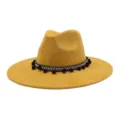 Detailed showcase of yellow suede fedora hat featuring black white band and pom poms. - Turmeric
