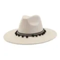 Detail view of beige suede fedora hat with black pom-pom band and wide brim design. - Beige