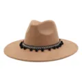 Detailed shot of camel suede fedora hat with black white geometric band and pom pom fringes. - Camel