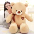 Detailed view of the giant plush teddy bear with brown ribbon bow and heart love patch. - Light Brown Heart Bear