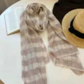 Detail view of a cozy plaid scarf in neutral tones, displayed neatly with chic lifestyle props. - Beige