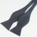 Close-up detail view of a solid black polyester self-tie bow tie for men formal business wear. - Dark Gray