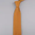 Primo piano di una cravatta in maglia giallo senape, con trama fine e dettaglio a punta. - Albicocca