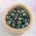 Close-up detail of glossy kiln-transformed ceramic beads in a natural straw nest for DIY crafts. - Golden Jade (Price per Piece)