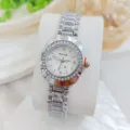Close-up detail of silver quartz wristwatch featuring a sparkling rhinestone bezel and white dial. - Silver White
