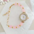 Detailed closeup of women pink beaded quartz watch with sparkly rhinestone dial and gold chain. - Pink