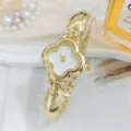 Golden clover dial watch detail closeup showing luxury metal link bracelet design style. - White