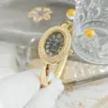 Closeup of a luxury gold-tone oval quartz bangle watch with dazzling crystal bezel and Roman numerals. - Rhinestone Style / Gold Black