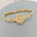 Detalle de un reloj de cuarzo dorado para mujer con bisel floral de estrás y pulsera de cristal. - Dorado