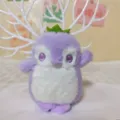 Primo piano del simpatico ciondolo in peluche di pinguino viola con occhi ricamati e corona. - Catena in ferro standard da 12 cm / Viola