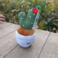 Gros plan d'un pendentif en peluche de cactus tricoté avec fleur rouge et pot, détail mignon. - Cactus