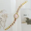 Detail der goldenen Quarz Damenarmbanduhr mit glänzenden Strasssteinen und lila Schmucksteinen. - Gold Violett