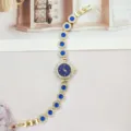Goldene Damenuhr Detail mit blauen Strasssteinen und elegantem dunklen Zifferblatt. - Goldblau