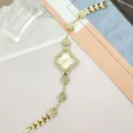 Gros plan des détails de la montre quartz femme strass trèfle dorée, bracelet étincelant. - Or Blanc