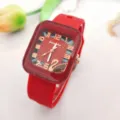 Détail du cadran carré à bracelet en silicone rouge avec chiffres dorés et motif de cygne. - Rouge