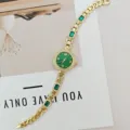 Elegante goldene Damen-Quarzuhr mit grünen Edelsteinen und funkelnden Strasssteinen am Armband. - Goldgehäuse Grünes Zifferblatt