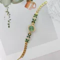 Nahaufnahme einer eleganten Damenquarzuhr in Gold mit grünen Steinen und glänzenden Kristallen. - Gold Grün