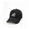 Nahaufnahme einer klassischen schwarzen Baumwoll-Baseballkappe mit weißem gestickten R-Logo. - Verstellbar / Schwarz