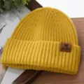 Close-up of yellow knitted beanie with brown leather tag, winter warm thermal cap details. - One Size / Yellow