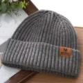 Nahaufnahme einer grauen Rippstrickmütze mit einem stilvollen braunen Lederaufnäher. - Einheitsgröße / Dunkelgrau