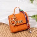 Mini llavero de bolso naranja elegante con herrajes dorados y bonito dije de cinta. - Naranja