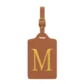Gros plan détail d'étiquette de bagage en cuir PU marron avec lettre M brodée dorée et boucle. - Lettre M