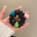 Close-up of fluffy winter wool hair scrunchie with colorful pom pom details on hand model. - Black