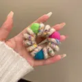Detailed close up view of colorful wool wrapped telephone cord hair tie with cute pom poms. - Off White