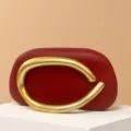 Detail view of the red mini evening bag featuring an oversized gold curved metal handle design. - Matte Handle / Dark Burgundy