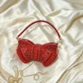 Close-up of red acrylic bow evening bag detail with sparkling rhinestones on luxury silk fabric. - Red