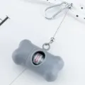 Grey bone-shaped pet waste bag dispenser with metal clip and retractable cord for outdoor dog walking. - Gray