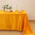 Vista dettagliata della tovaglia in raso giallo con consistenza liscia e drappeggio. - Oro
