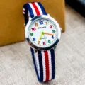 Kinder Quarz-Uhr mit bunten Ziffern, blau rot weisses Nylonarmband und weisses Zifferblatt. - Kleine rote Farbzeiger