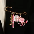 Dettaglio di una spilla a balia marina con ciondoli granchio e perla su un blazer. - Oro KC