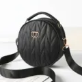Black round quilted crossbody bag with chic chevron pattern and stylish wide shoulder strap. - Black