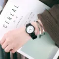 Detailaufnahme einer minimalistischen Quarzuhr mit schwarzem Armband am feinen Handgelenk. - Kleine Uhr mit weißem Zifferblatt und Ziffern