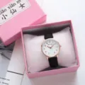 Minimalist quartz wrist watch detail with black strap and white dial in a pink gift box. - Black