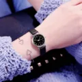 Nahaufnahme Detail der Damen kleiner Zifferblatt Quarzuhr mit Lederarmband und Armreif. - Schwarzes Armband Schwarzes Zifferblatt