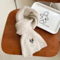 Gedetailleerd opname van een gezellige beige gebreide wintersjaal met schattig hond borduurwerk. - Beige
