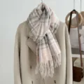 Detailed view of a cozy pink and grey plaid scarf with fringe hanging on a stylish winter coat. - Picture Color 7
